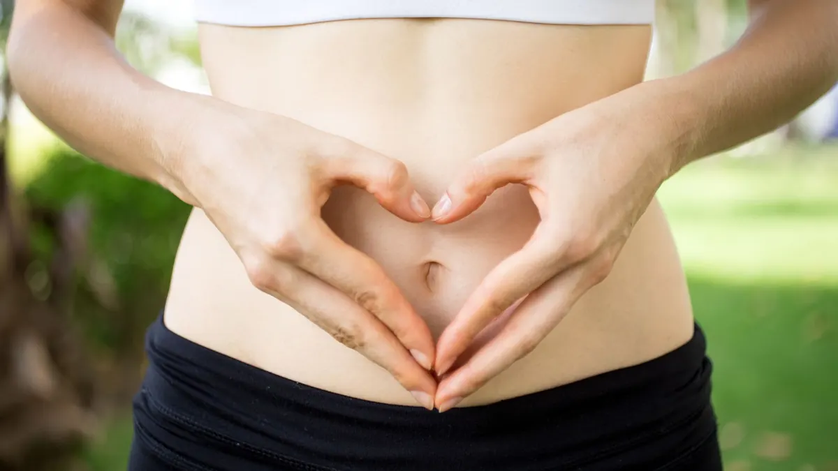 Mulher fazendo sinal de coração em frente ao abdômen