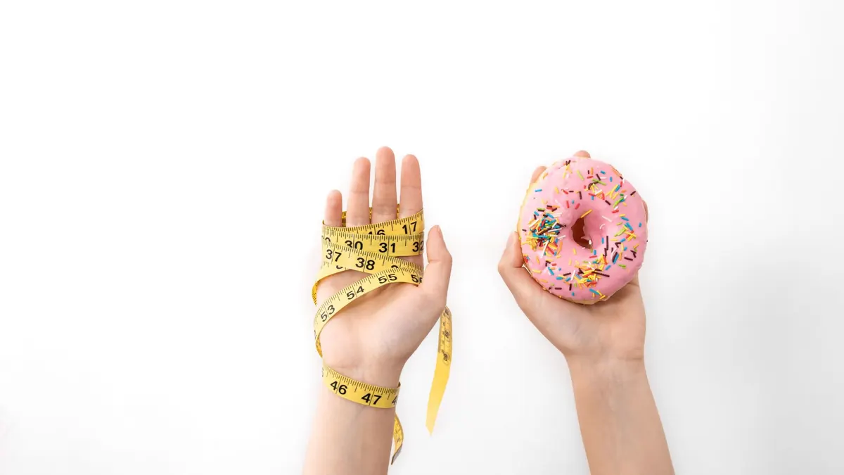 Mãos segurando donut e fita métrica em fundo branco