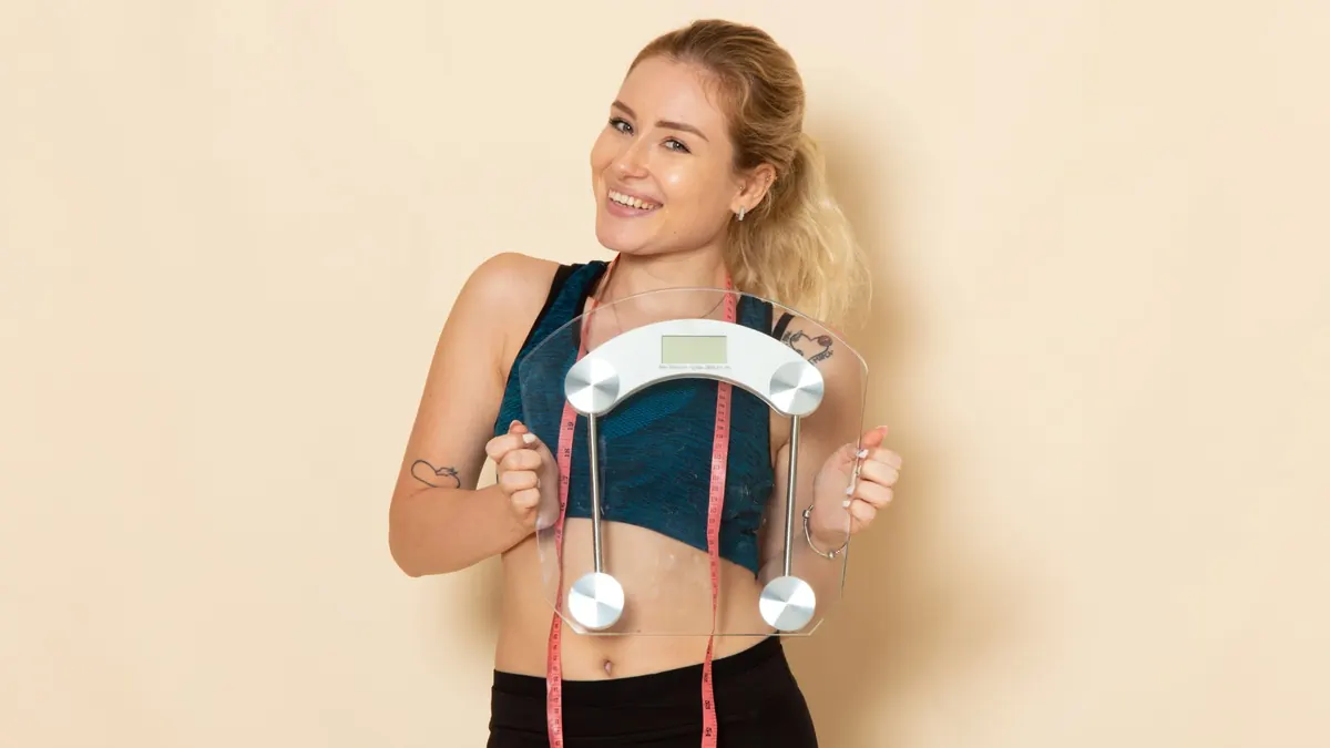 Mulher jovem fitness segurando balança e sorrindo