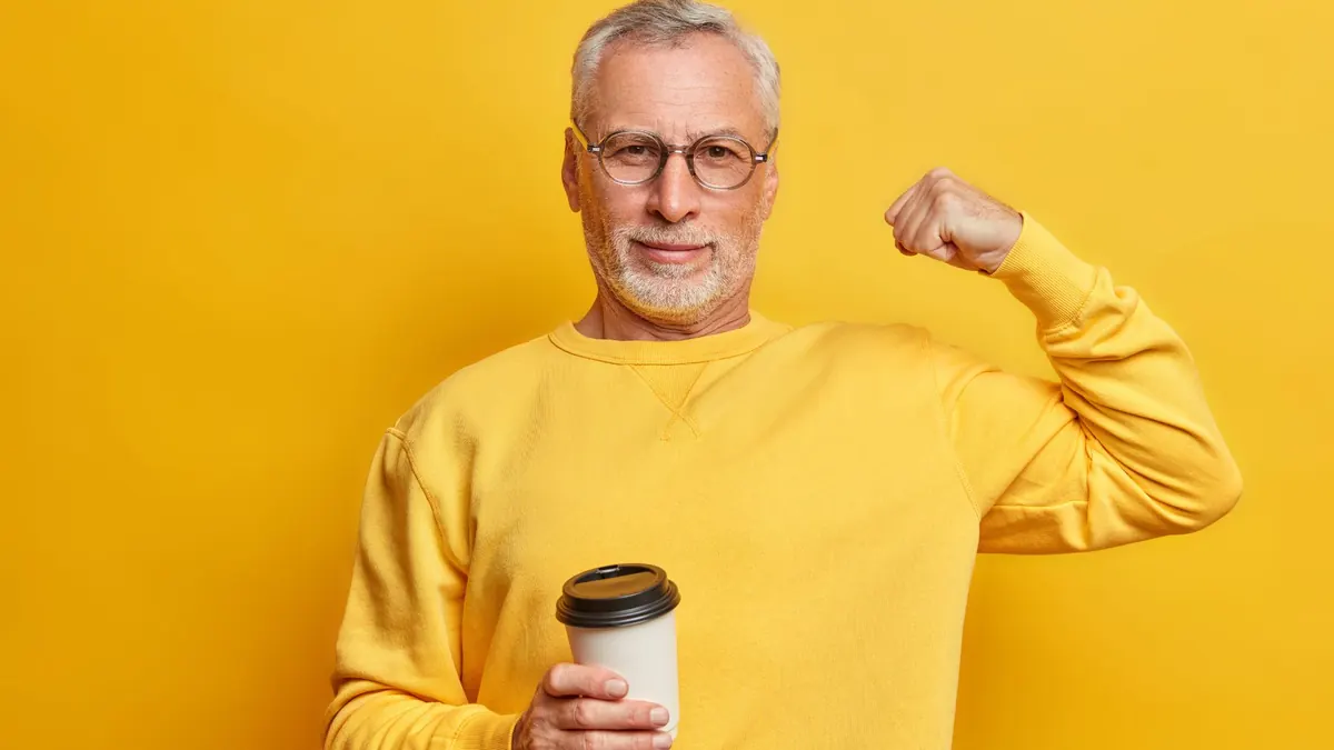 Homem mostrando bíceps com copo de café em fundo amarelo