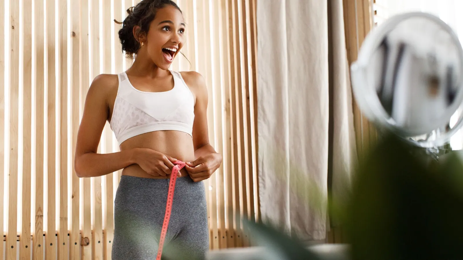 Mulher medindo a cintura com fita métrica e sorrindo