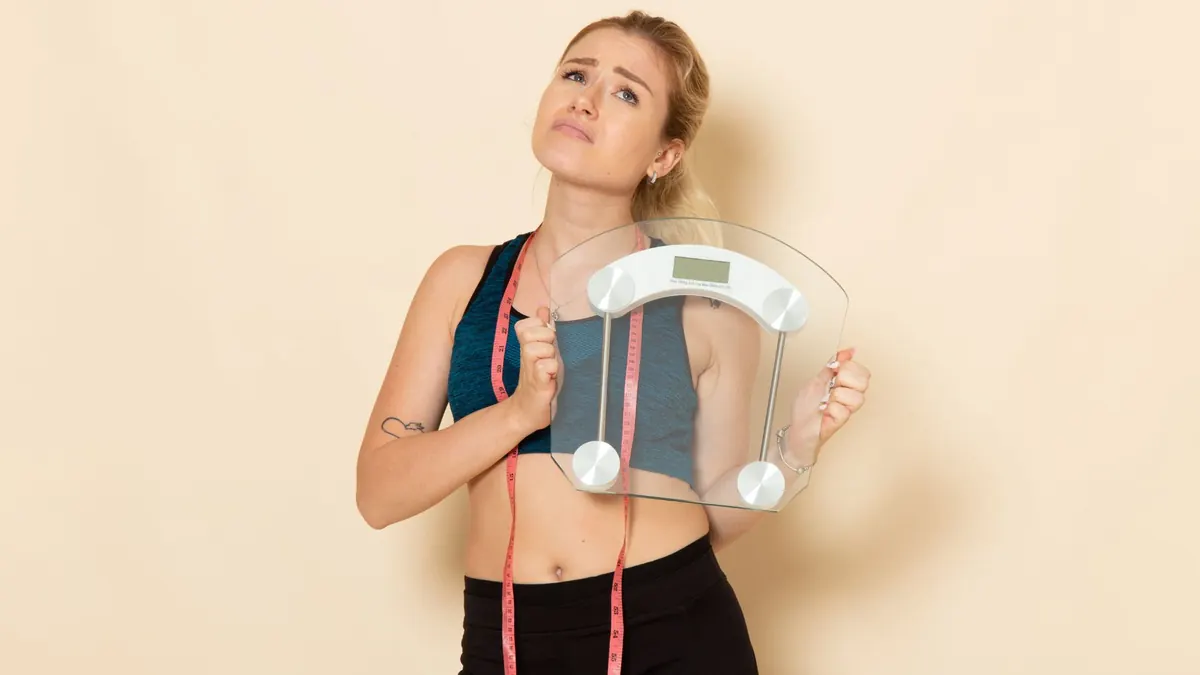 Mulher fitness segurando balança em fundo branco